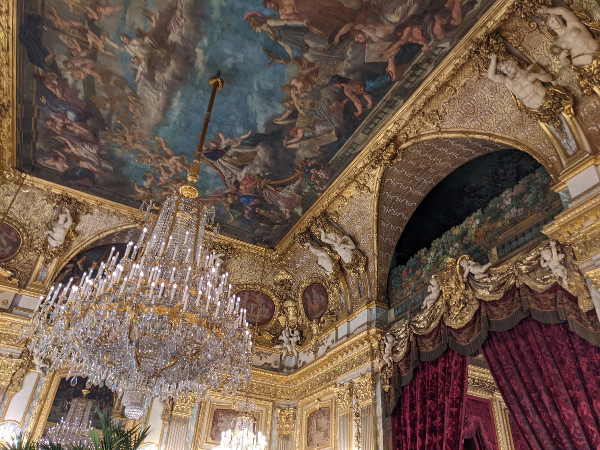 Decorative ceiling art and a chandelier inside the Louvre Museum