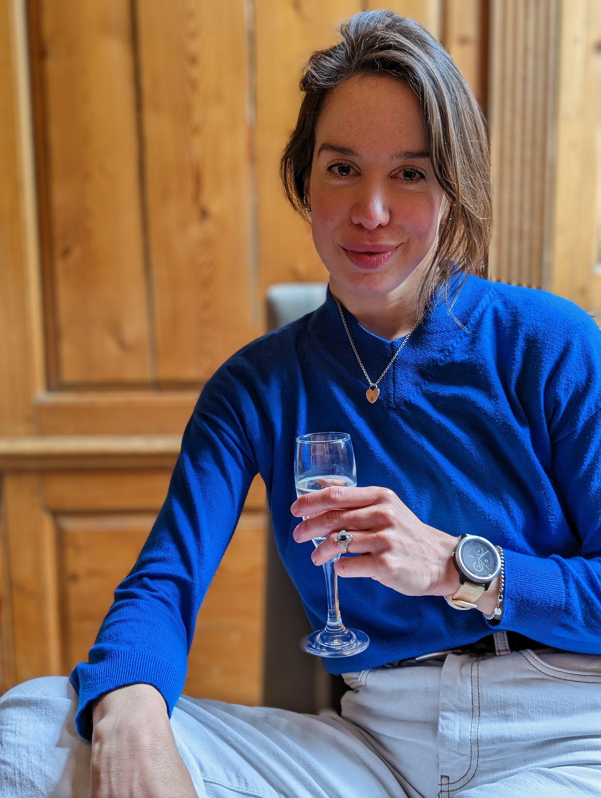 A women in a blue jumper holds a glass of prosecco. 
