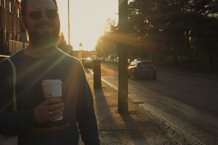 Man with a beard in his thirties wearing dark sunglasses holds a coffee in Norwich, Norfolk, 2022