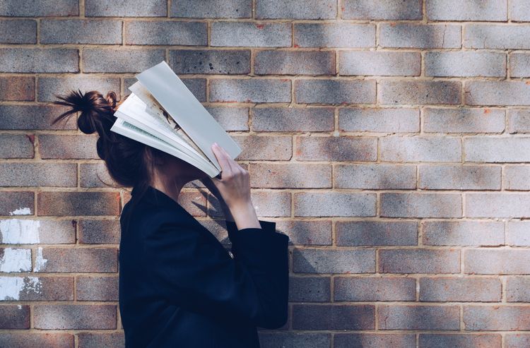 Women next to brick wall hits her head with a book in frustration