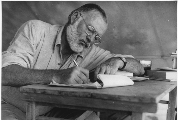 Ernest Hemingway writing at his desk in a campsite in Kenya, circa 1953