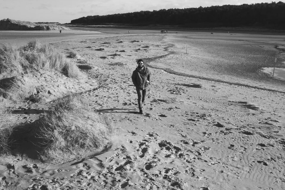Black and white photo of a man with beard walking on Holkham Beach in north Norfolk