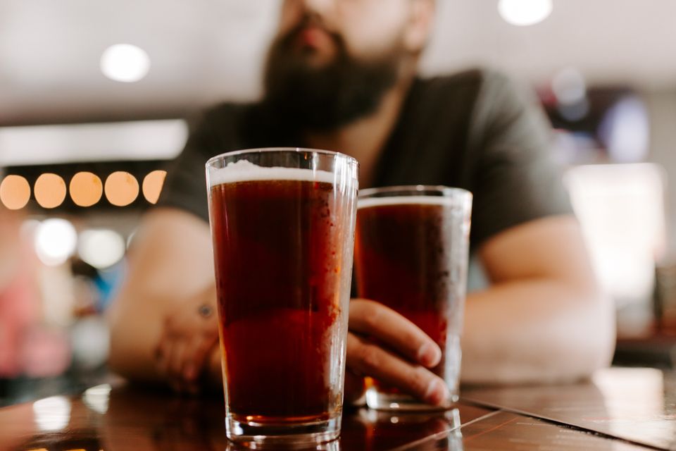 Man with a beard at a bar with two pints